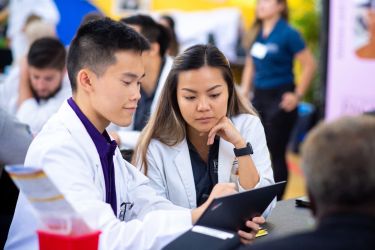 Students in white coats looking at laptop.