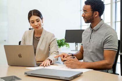 Two people sit at a desk looking at a computer together