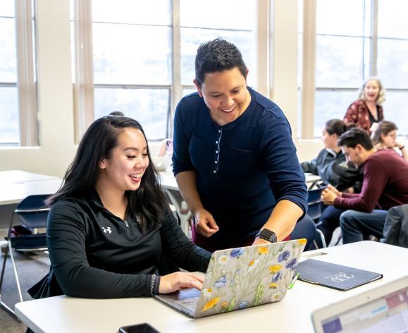 education professor with student in classroom looking at laptop