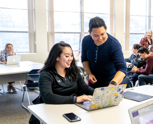 education professor with student in classroom looking at laptop